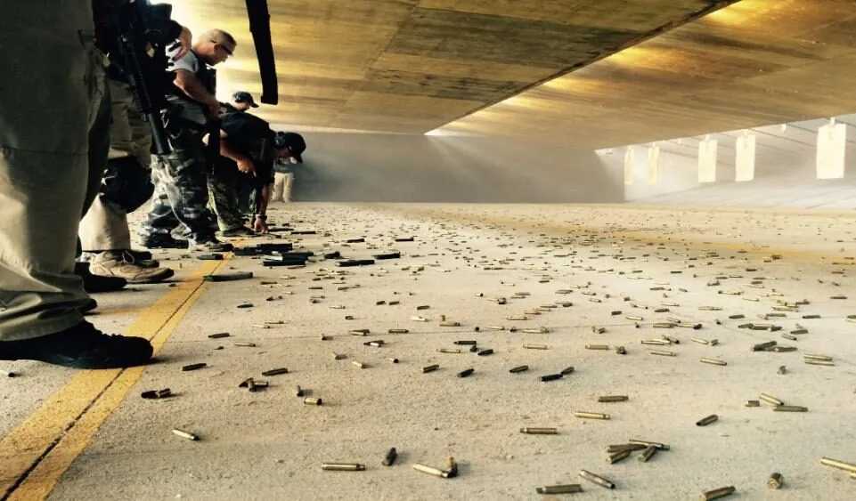 People practicing at an indoor shooting range with scattered bullet casings.