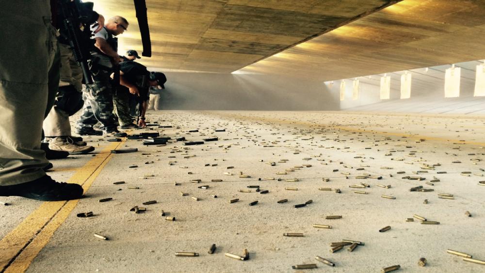 People practicing at an indoor shooting range with scattered bullet casings.