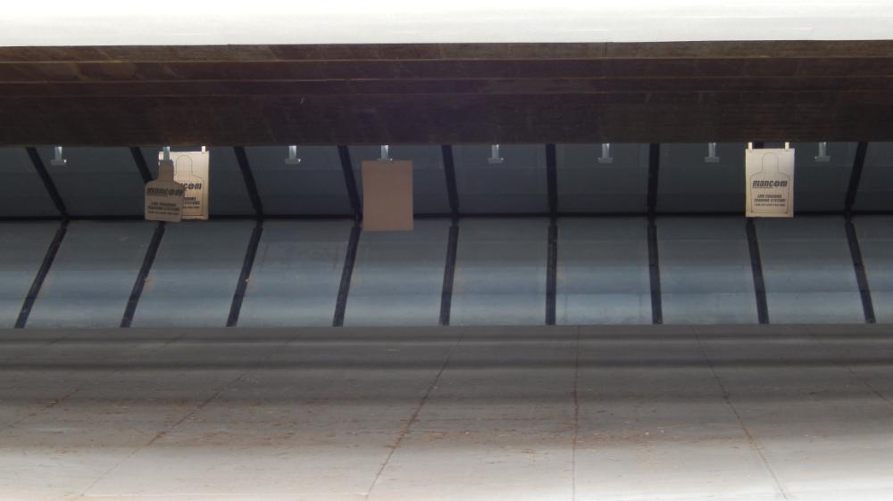 Indoor shooting range with three target boards hanging.