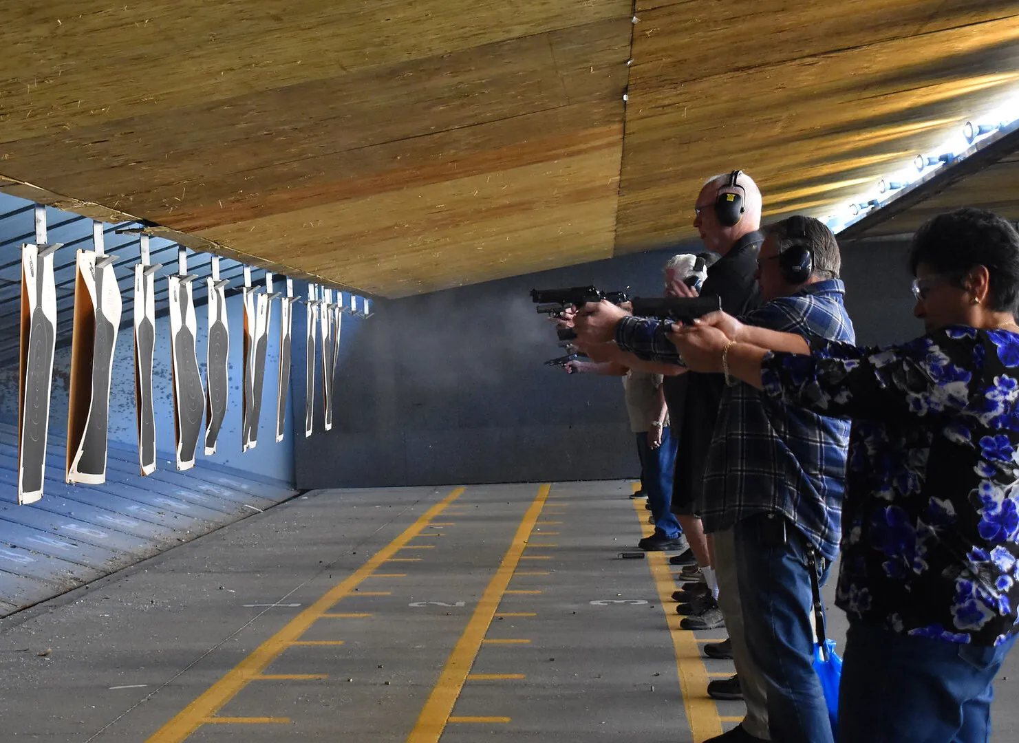 People at indoor shooting range aiming handguns at paper targets