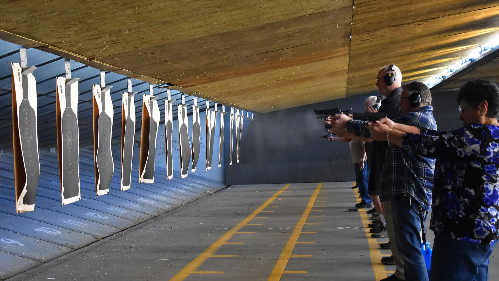 People at indoor shooting range aiming handguns at paper targets