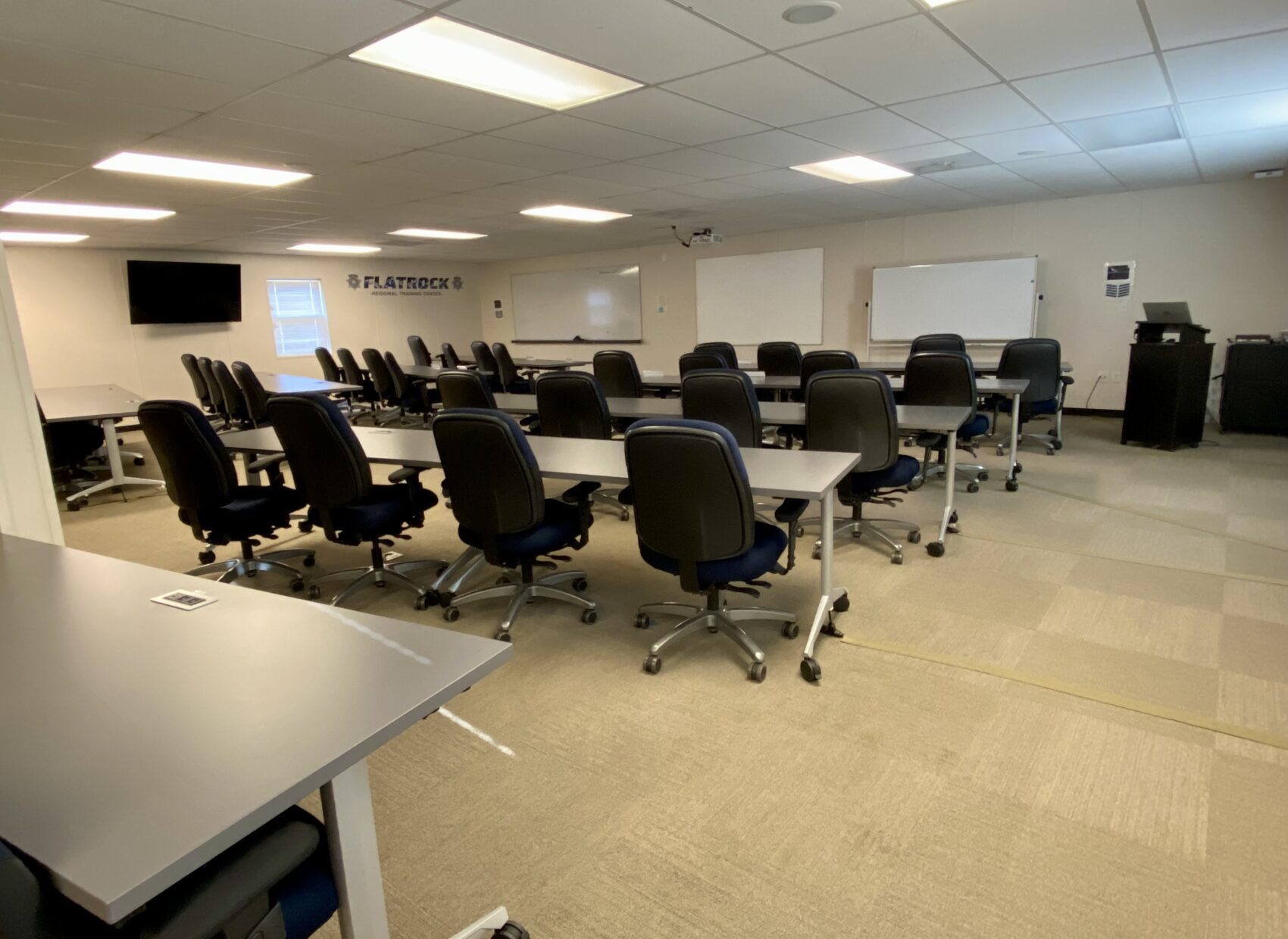 Classroom setup with rows of tables and chairs, whiteboards, and a screen, showcasing a learning environment.