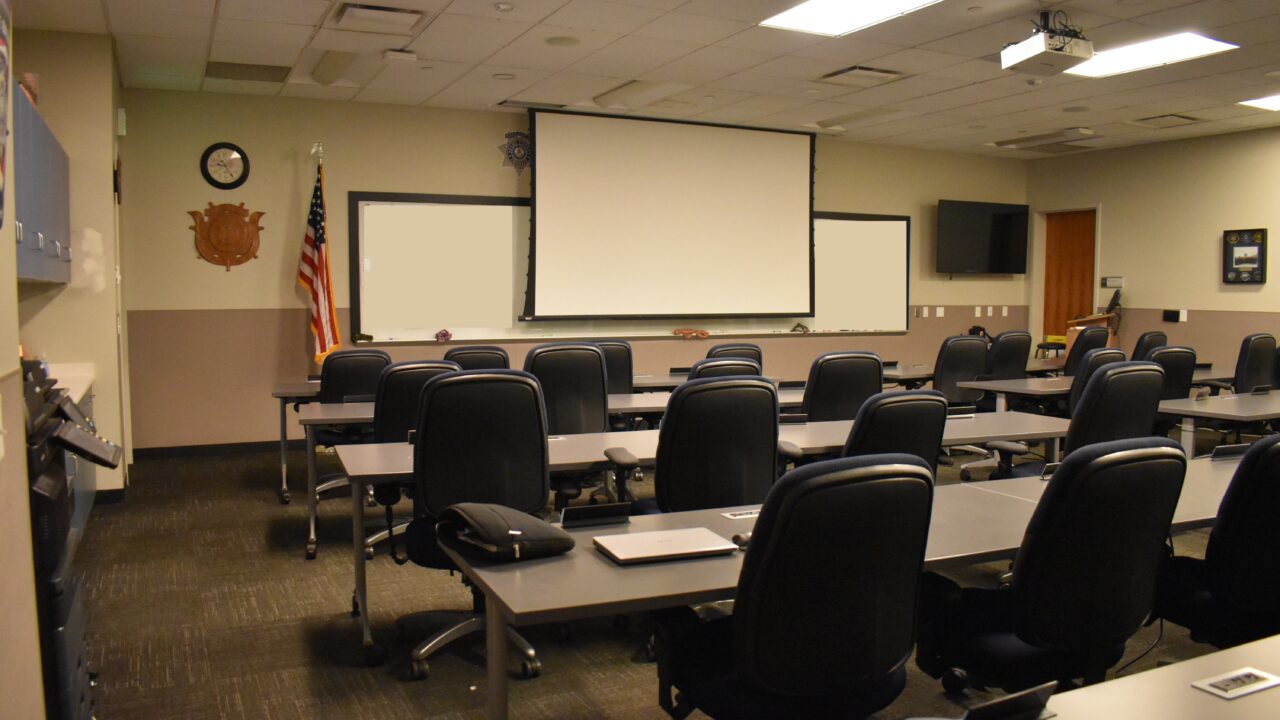 Empty classroom with rows of chairs, projector, and American flag