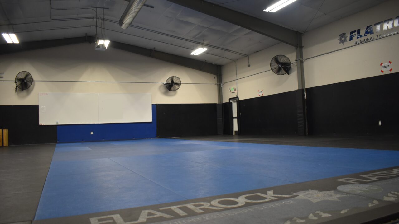 Martial arts training room with blue mats and wall fans, "FLATROCK" text visible.