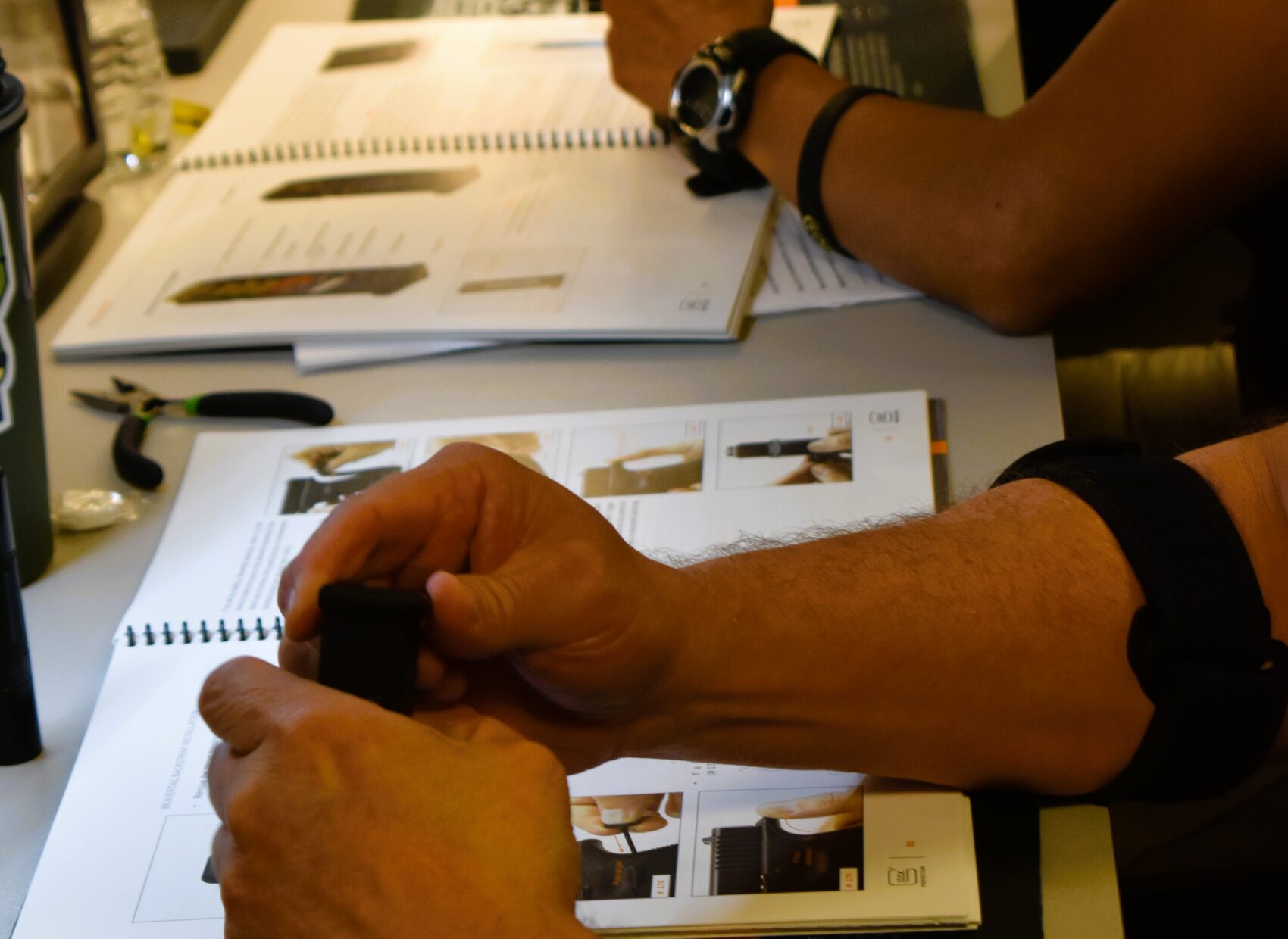 Hands assembling a small device during a course, manuals open on table