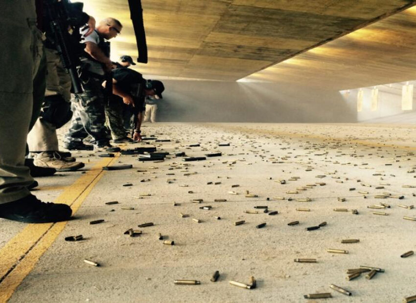 A group of officers at an indoor firing range, scattered bullet casings on the ground.