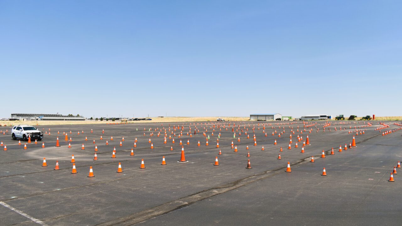 Open parking lot with numerous orange traffic cones and a lone SUV navigating through.