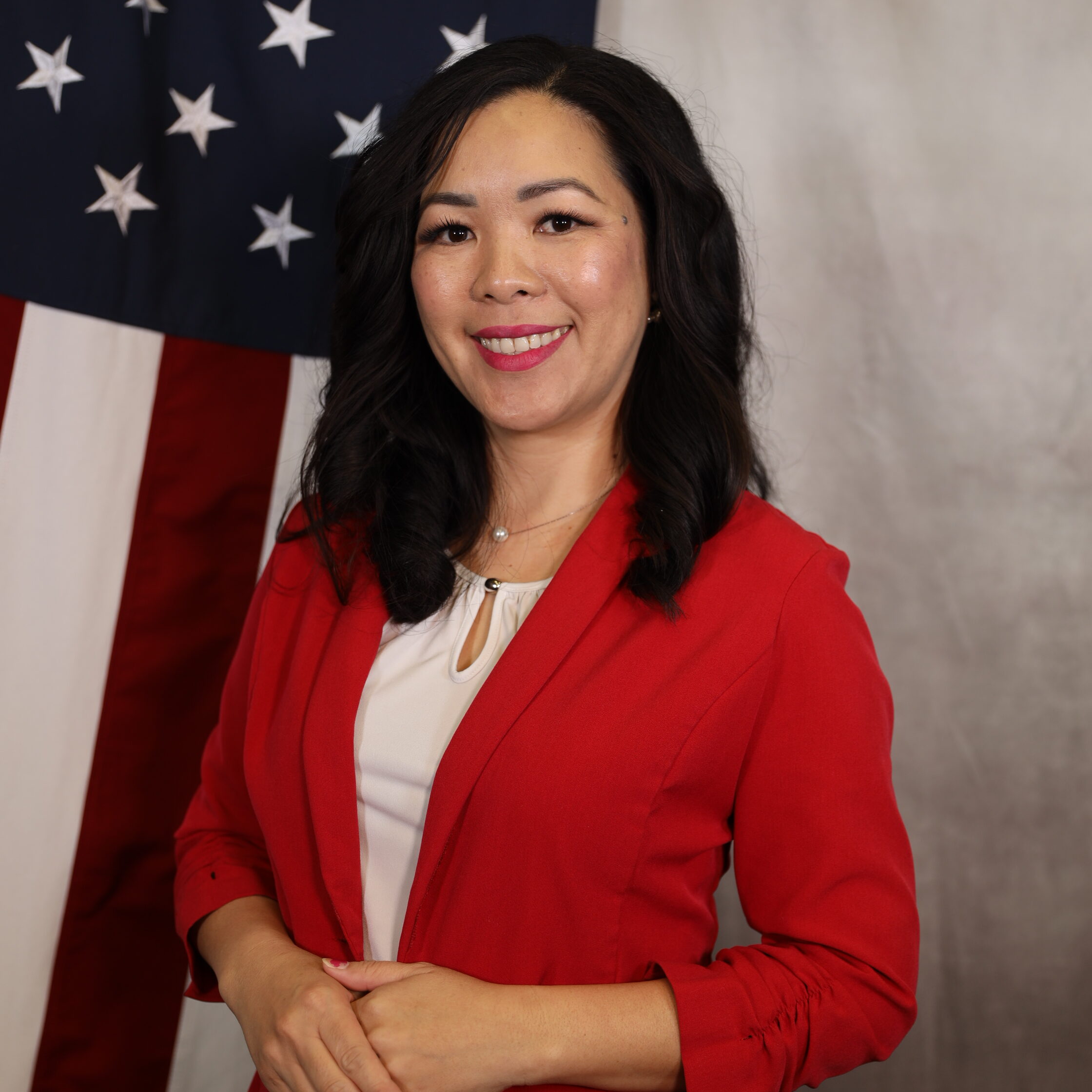 Yang-Trace.jpg: Woman in red blazer smiling, standing beside U.S. flag.